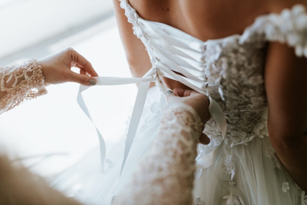 Close-up of hands lacing the ribbon corset of a bride's lace wedding dress