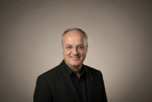 Portrait of Predrag Canjko, General Manager of SPA Hotel Kanin Bovec, in a dark jacket against a warm grey backdrop