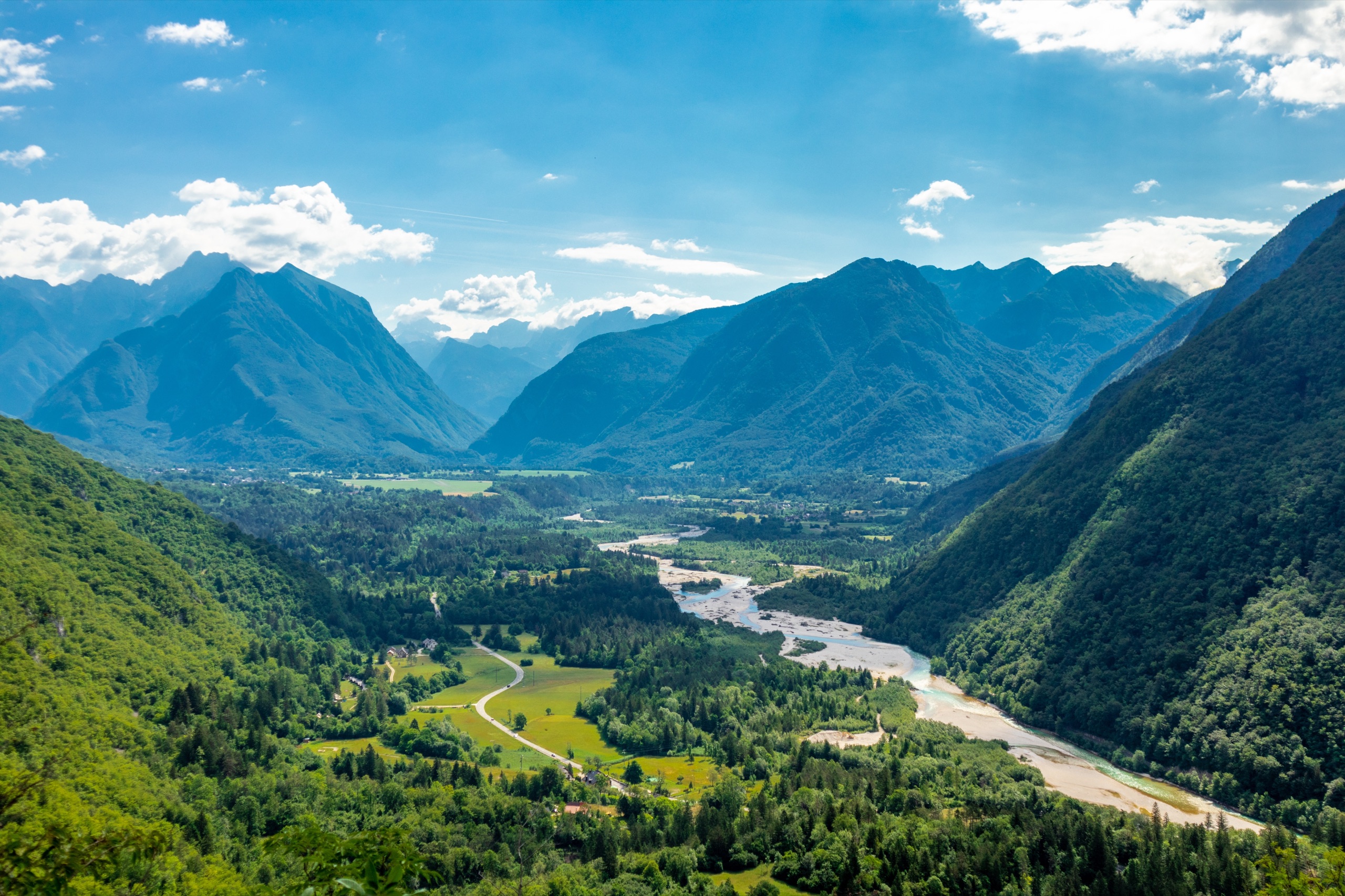 Green valley with a braided river winding between forested mountains under a blue sky with clouds