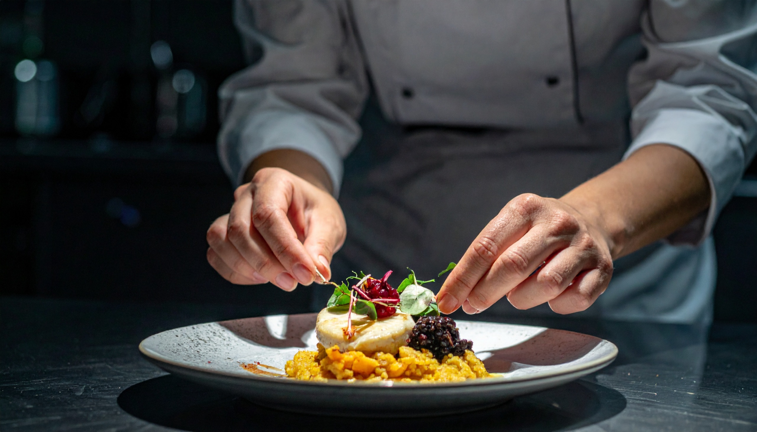 Chef garnishing a plate of risotto topped with fish, beetroot and microgreens