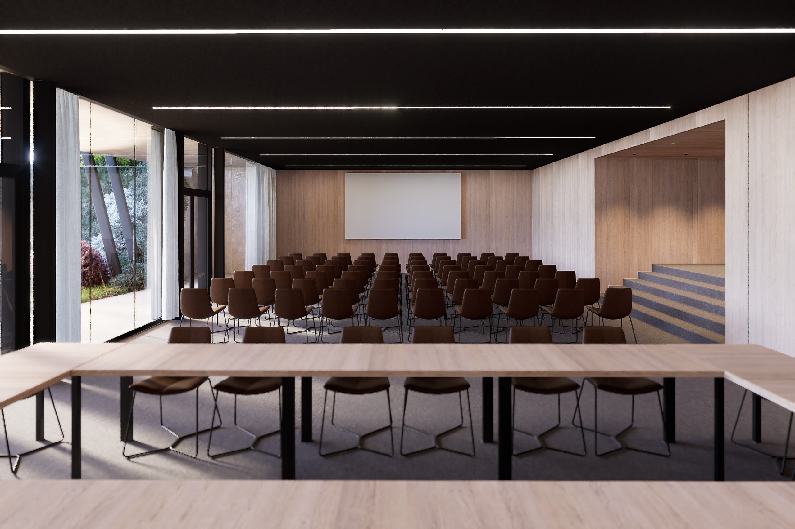 Event hall with rows of chairs facing a projection screen, a U-shaped table in front and glass walls onto greenery